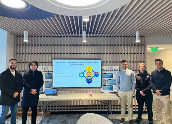 5 male students posing in front of a presentation on a screen