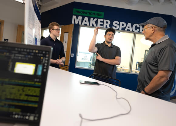 Students presenting their poster with a computer screen showing code in the bottom left-hand corner
