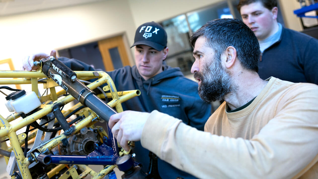 2 students and a professor work on the baja vehicle